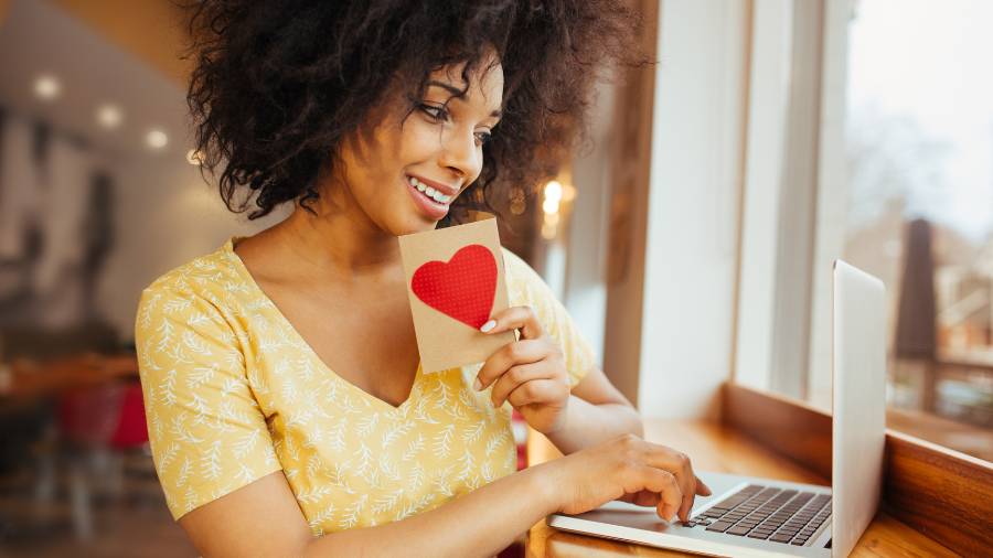 Woman on laptop holding a heart sign.