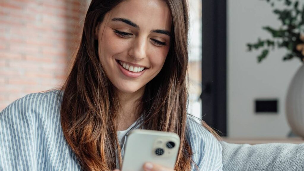 Smiling woman looking at smartphone screen, sitting on couch