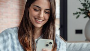 Smiling woman looking at smartphone screen, sitting on couch