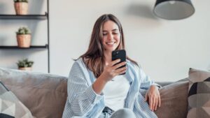Smiling woman looking at smartphone screen, sitting on couch, en