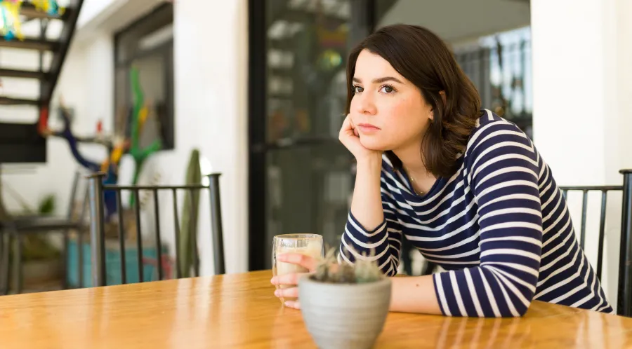 An adult feeling lonely while dating, sitting beside a window with a phone and a mug.